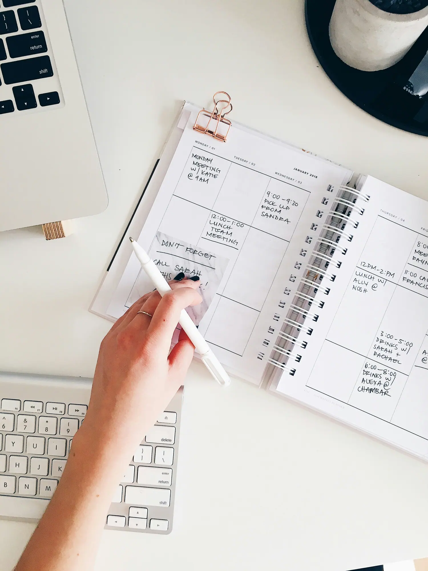 Une main note un planning dans un carnet posé sur un bureau blanc